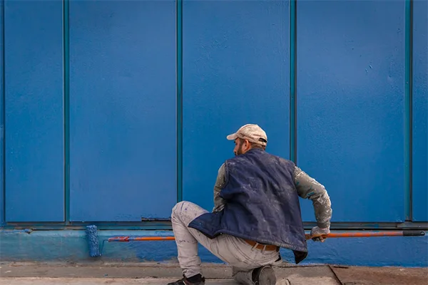 A construction worker paints a large blue wall outside, adding color and life