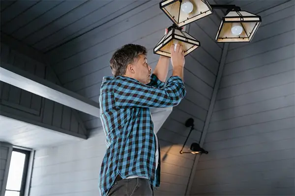 A man in a plaid shirt changes a light bulb on a ceiling lamp in a stylish modern interior
